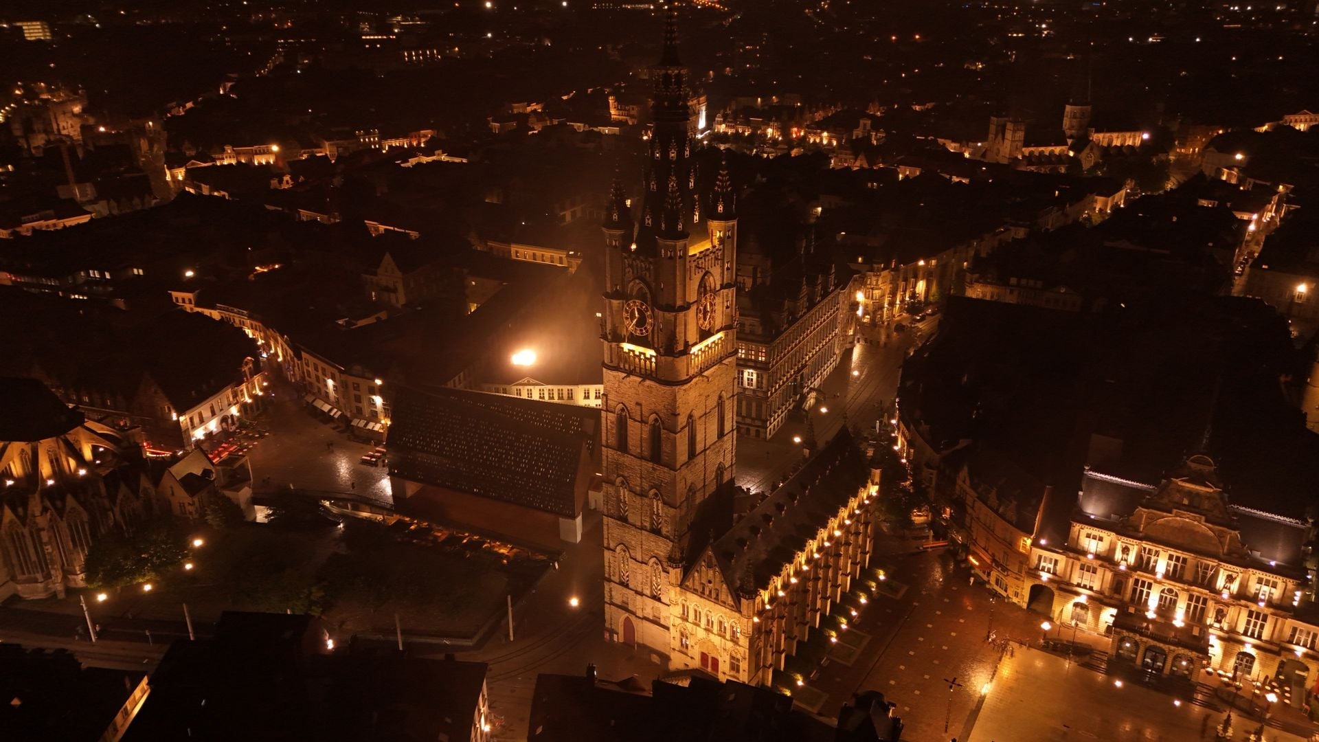 Aerial birds-eye view of a historic European city square and cathedral at night, softly illuminated by warm, non-glaring amber municipal streetlights that minimize urban light pollution
