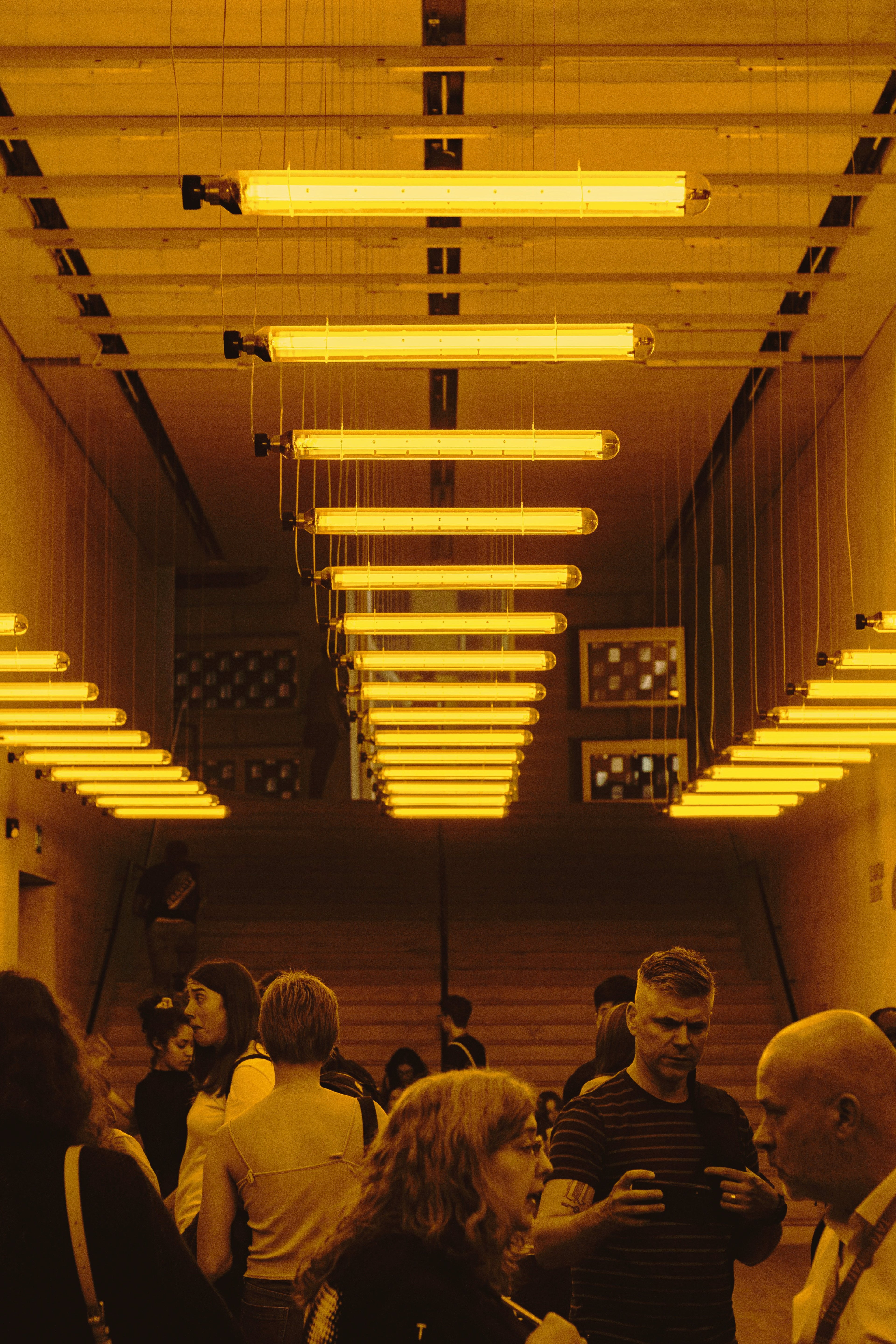 An indoor art gallery installation utilizing classic Philips SOX low pressure sodium lamps, capturing the distinct 589nm monochromatic amber glow that alters human color perception and creates high-contrast grayscale effects.